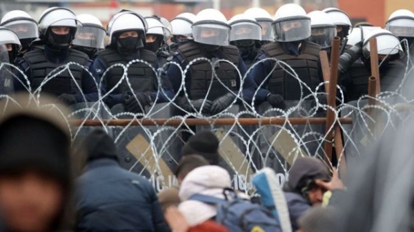 Polish police officers and migrants face each other across barbed wire, 2021